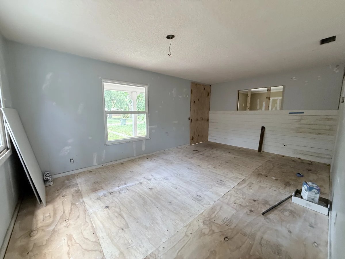 Empty room in a Florida house during repairs, with bare plywood floor and open wall framing